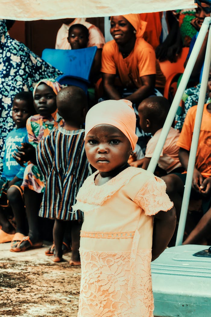 A young girl stands amidst a community gathering in Nalerigu, Ghana, showcasing vibrant traditional attire and culture.